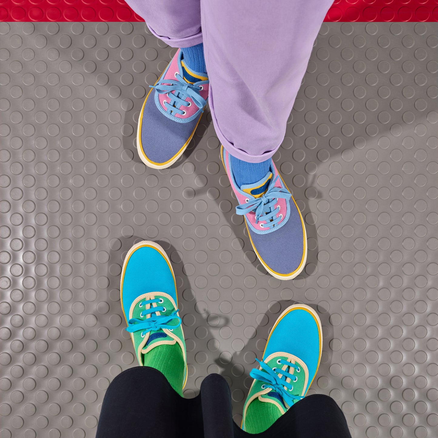 Two pairs of frisky and colorful shoes on a textured floor.